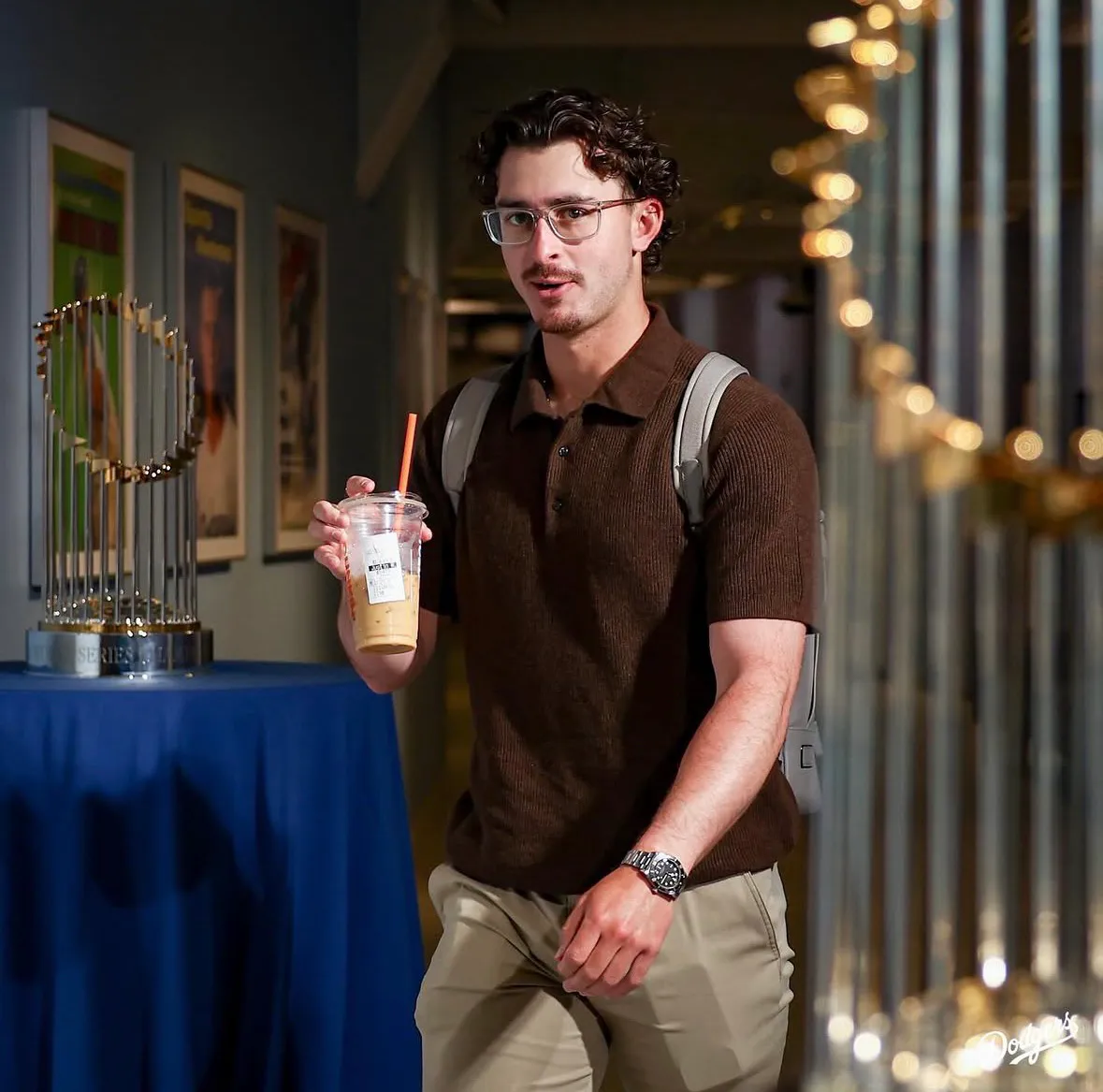 Justin looks like he’s gotten a perm. Whatever. Chocolate brown polo and tan khakis with an emotional support coffee, as always. 
